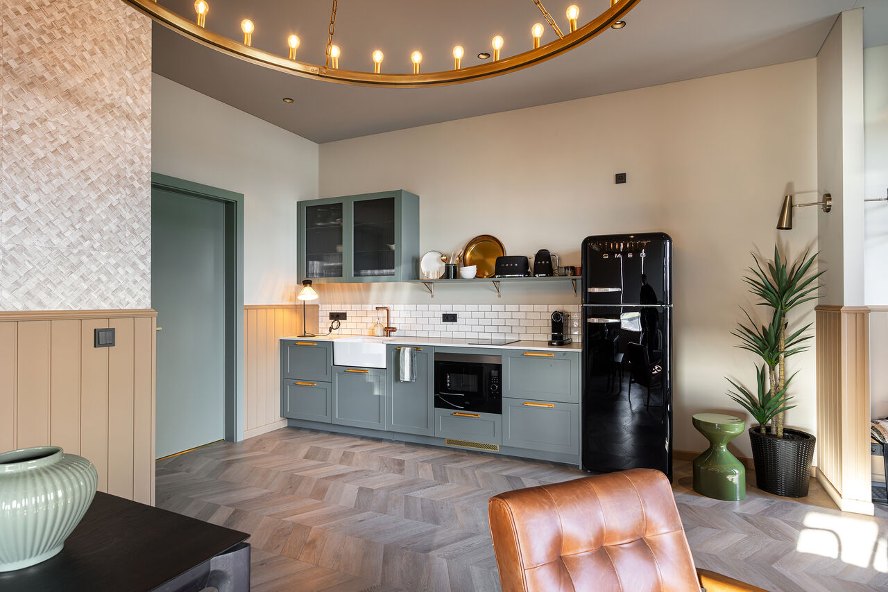 A sage-green kitchen with a black retro fridge in a one-bedroom apartment